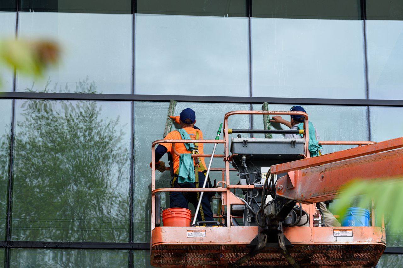 Deux ouvriers lavant les fenêtres d’une façade en verre à l’aide d’une nacelle, pour améliorer l’apparence du bâtiment.
